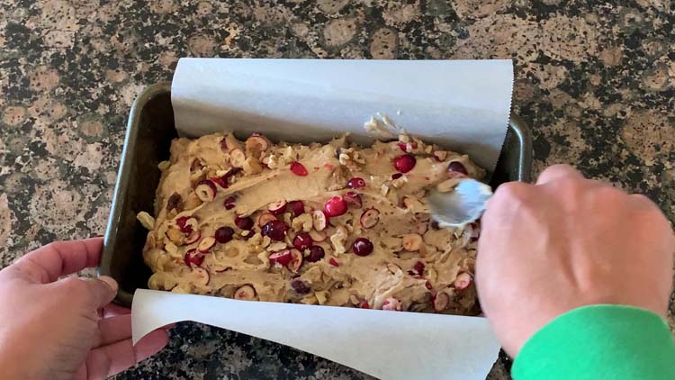 Using a spoon to level off the Cranberry bread dough in a loaf pan
