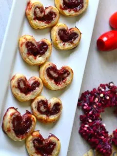 valentine palmiers arranged in a rectangular white plate with a red berry wreath nearby.