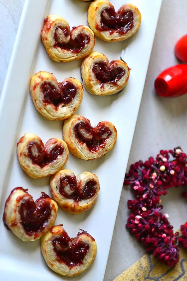 valentine palmiers arranged in a rectangular white plate  with a red berry wreath nearby.
