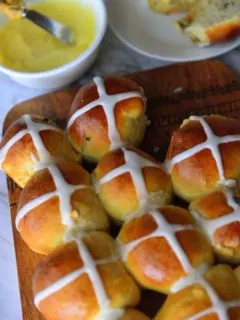 Hot Cross buns on a board with butter in a bowl next to it.
