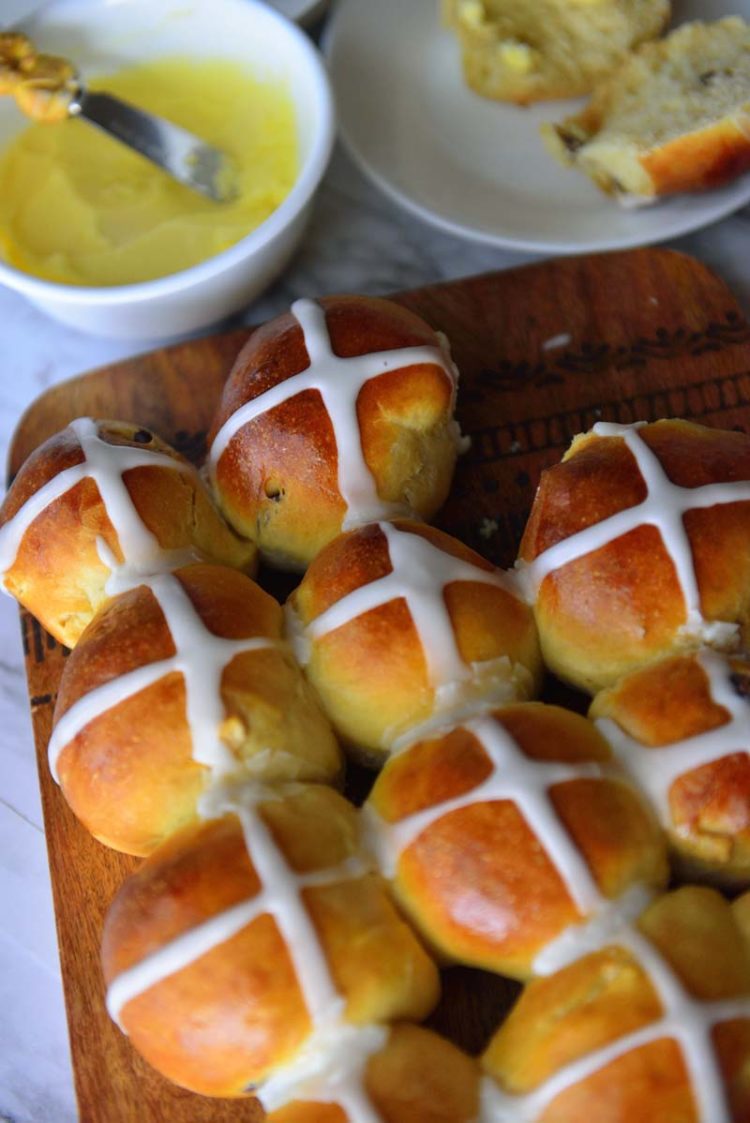 Hot Cross buns on a board with butter in a bowl next to it.