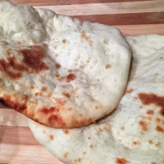 two Naan breads on a wooden board.