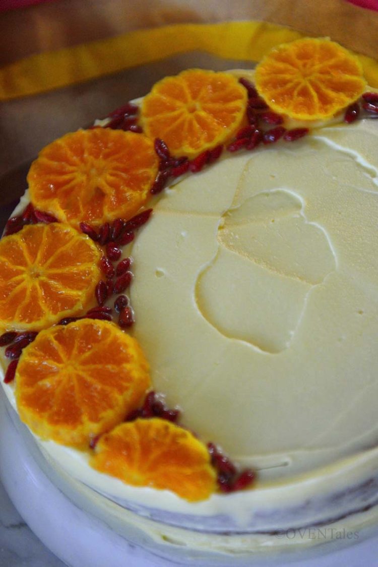 Cake decorated with orange slices and red berries on a stand.