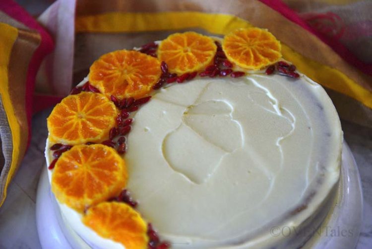Cake decorated with orange slices and goji berries on a stand.