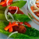 Image for pinterest - tuna cutlets on lettuce leaves with onion and onion and bell pepper salad.