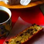 A slce of plum cake on a wax paper with a mug of coffee next to it. Caption - Easy Plum Cake
