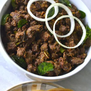 Nadan Beef Ularthiyathu in a white bowl with few onion rings on top