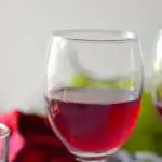 A glass of red wine and with a red glitter flower in the back ground. Caption - Home Made Grape Wine. Image for pinning