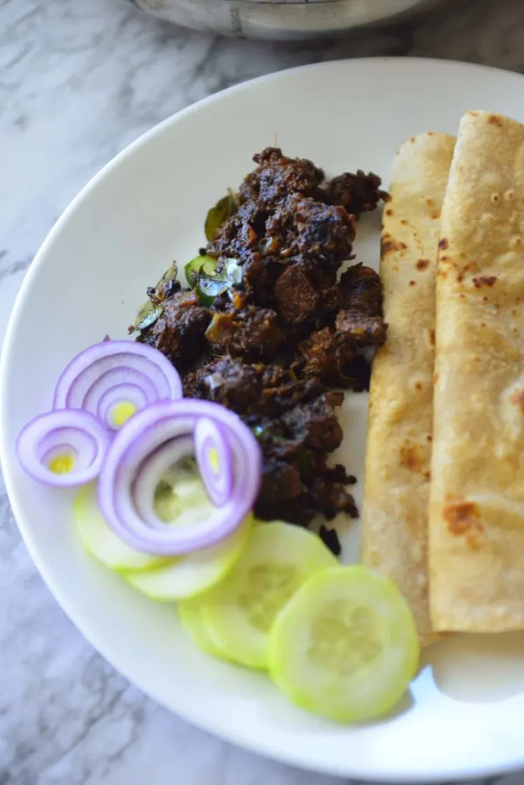A plate with flatbreads, beef fry  and a few slices of cucumbers and onions