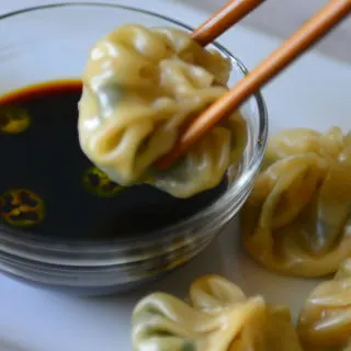 Closeup of momo held on chopsticks about to be dippedinto sauce