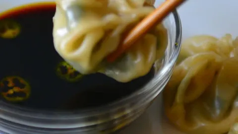 Closeup of momo held on chopsticks about to be dippedinto sauce