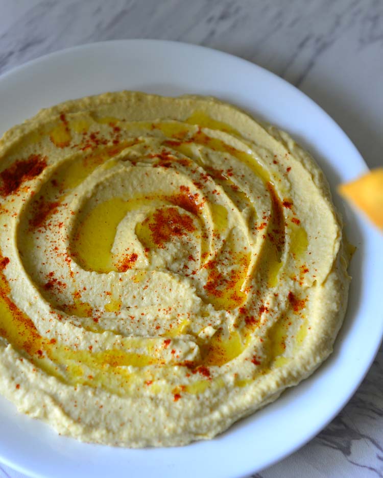 Hummus spread on a white plate with olive oil drizzled on top and  a sprinkling of paprika
