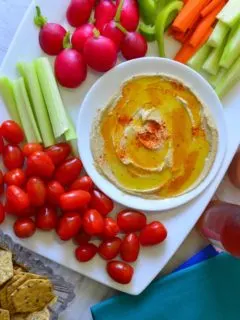 Home made hummus served with fresh veggies and crackers on a white platter