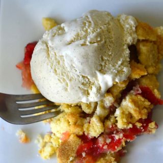 A fork scooping Strawberry Rhubarb Crumble on a white plate.