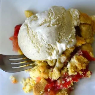 A fork scooping Strawberry Rhubarb Crumble on a white plate.