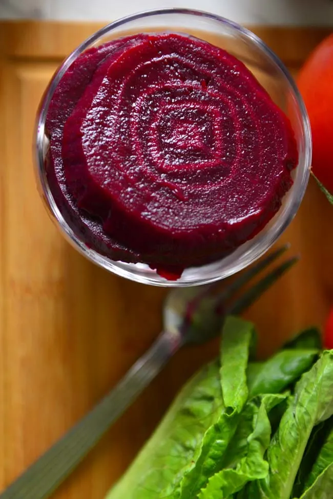 A bowl of Pickled Beets on a wooden board  with a head of lettuce next to it.
