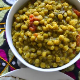 Peas curry in a white bowl along with a platter of bread.