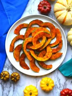 Hot And Sweet Roasted Kabocha squash on a marble patter with mini gourds surrounding it.