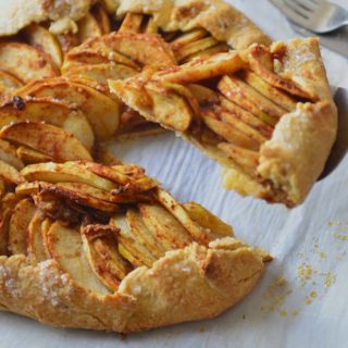 Apple galette on a parchment paper with a lice on pie server