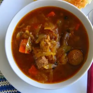A bowl of Bigos -or the meat stew - on a plate with a slice of crusty bread on the side