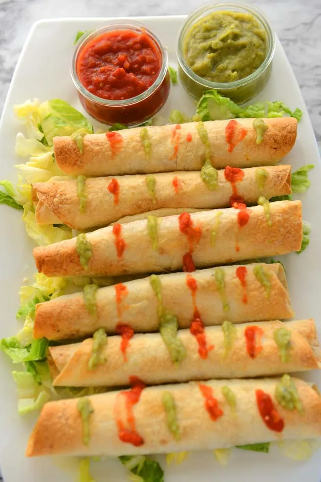 Flautas on a white plate  with green and  red salsa 