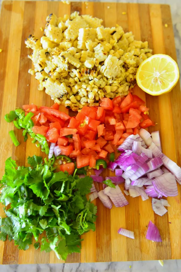 Grilled corn kernels, chopped tomatoes, onions, chilies and cilantro , and a slice of lemon for making the grilled corn salsa 