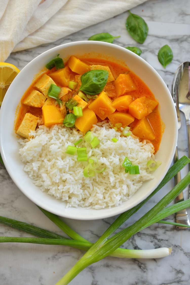 A bowl of rice and squash curry garnished with few scallions and basil leaves