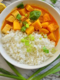A bowl of rice and squash curry garnished with few scallions and basil leaves