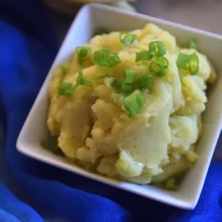 Mashed potatoes with scallions sprinkled on top in a white bowl