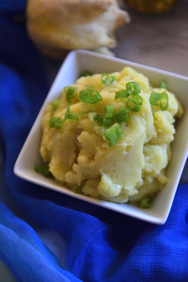 Mashed potatoes with  scallions sprinkled on top in a white bowl