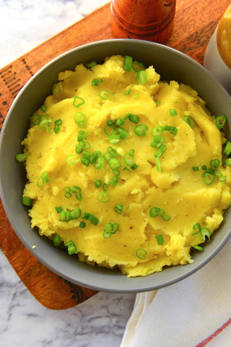 Golden mashed potatoes in a grey bowl set on a wooden board
