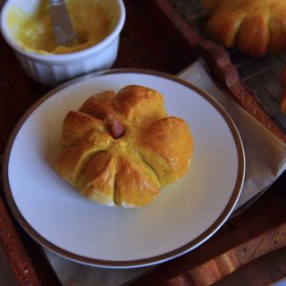 A pumpkin shaped roll on a plate with a bowl of spread next to it