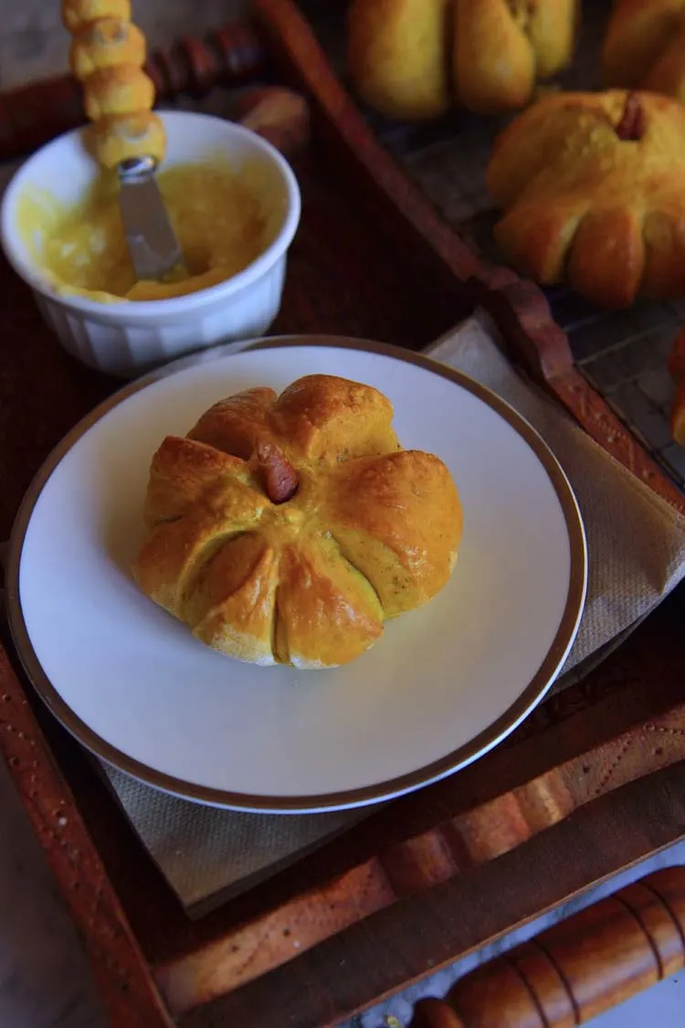 A pumpkin shaped roll on a plate with a bowl of spread next to it
