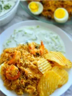 Shrimp biryani and cucumber raita in a white plate with some chips