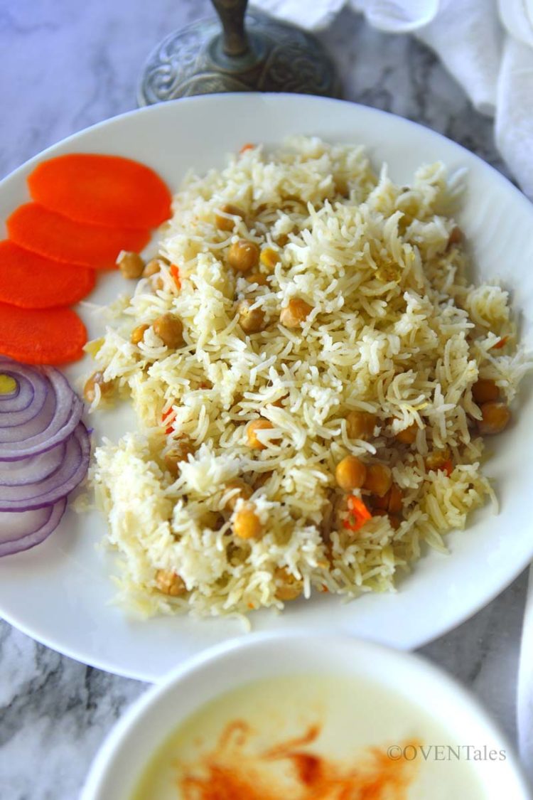 Chickpea pilaf in a white plate with slices of onions and carrots. A bowl of chutney next to it.