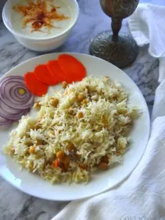 A plate with rice and with a bowl of raita and a silver chalice next to it.