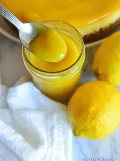 Scooping lemon curd from a bottle to show the texture, and lemons and tart next to it.