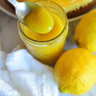 Scooping lemon curd from a bottle to show the texture, and lemons and tart next to it.