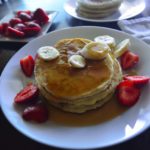 Stack of pancakes on a plate with fruits and syrup.