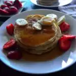 Image for pinning - stack of pancakes on a white plate with syrup and sliced fruit on it.