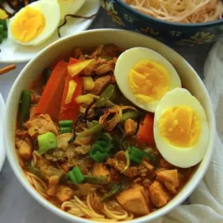 A white noodle bowl filled with Khow suey with various toppings